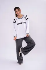 Buzo estilo jersey universitario de color blanco con detalles en negro. Presenta cuello en V, mangas largas con franjas negras y un número estampado en la espalda. Confeccionado en tela deportiva, con corte holgado y puños acanalados.