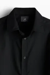 Camisa H&M de manga larga, color negro, con cuello inglés, cierre frontal de botones y corte regular fit.