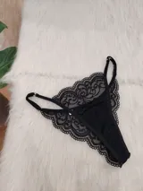 Tanga colaless de encaje negro con diseño floral, breteles regulables y herrajes metálicos.