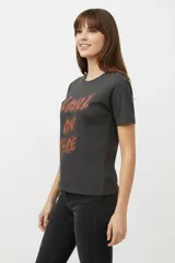 Remera de algodón negra de manga corta y cuello redondo, con estampa frontal que incluye letras rojas y gráficos en tonos dorados.