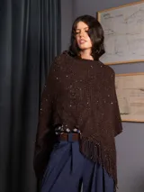 Poncho tejido de punto color marrón, con diseño asimétrico, detalle de lentejuelas sutiles y flecos en el borde inferior.