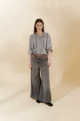 Pantalón de jean gris oscuro, estilo sastrero de tiro medio bajo y corte ancho (wide leg). Presenta costuras marcadas en el frente y un cinturón trenzado marrón con hebilla metálica.