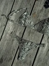 Conjunto de bikini con estampado de piel de serpiente en tonos grises y negros. El top es de estilo triángulo fijo con breteles regulables y cierre de gancho en la espalda. La bombacha es de corte vedetina con laterales fruncidos elásticos.