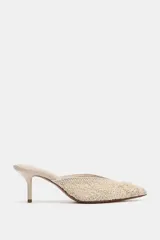 Zapato mule destalonado color crudo, con tacón fino alto, punta fina y cuerpo con bordados texturizados y apliques de cuentas.