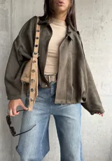 Campera tipo bomber de gamuza color verde, con diseño oversize, cuello camisero, cierre frontal y detalles de charreteras en los hombros.