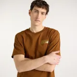 Remera marrón de manga corta de New Balance, con corte amplio y relajado, cuello redondo y gráfico pequeño de la marca en el pecho.