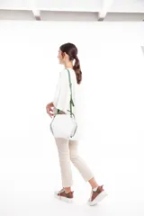 Bolso bandolera de cuero sintético blanco, lila y verde, con forma hexagonal y correa larga verde ajustable.