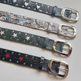 Cinturón de cuero negro con textura de cocodrilo, tachas metálicas plateadas y apliques en forma de estrella. Incluye hebilla cuadrada de metal plateado.