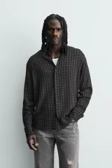 Camisa de corte relajado con diseño de cuadros en tonos negro y beige, cuello camisero, manga larga y cierre frontal de botones.