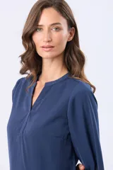 Blusa de manga larga en color azul marino, con escote en V y diseño de doble capa en el frente. Presenta puños elásticos y un pequeño aplique metálico decorativo en el ruedo.