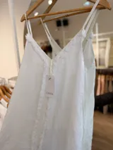 Vestido maxi de lino color blanco, con escote en V, tirantes finos regulables y detalles de flecos en el frente.