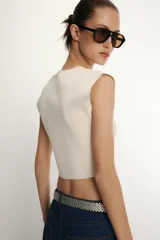 Top corto de punto color beige claro, con cuello redondo y mangas cortas tipo hombrera.