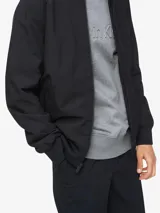 Campera bomber negra Calvin Klein de poliéster y algodón, con cuello redondo, cierre frontal, bolsillos laterales con cierre, logo en el pecho y ribete de punto acanalado.