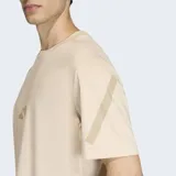 Remera de algodón color beige con cuello redondo y mangas cortas. Presenta el logo de Adidas estampado en el centro del pecho en un tono más oscuro y detalles gráficos en las mangas.
