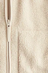 Campera de sherpa suave con cuello elevado, cierre frontal y bolsillos laterales de parche. Presenta un diseño de hombros caídos y corte holgado.