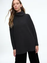 Sweater de silueta amplia y corte holgado, confeccionado en tejido de punto color gris oscuro. Presenta cuello polera, mangas largas con ajuste en los puños y diseño contemporáneo.