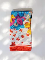 Pañuelo cuadrado de seda con estampado floral multicolor que combina tonos rojos, amarillos, azules y fucsias sobre fondo blanco, con borde rojo.