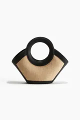 Cartera de mano con cuerpo de paja trenzada y detalles en cuero sintético negro. Presenta un diseño estructurado con asas circulares integradas y cierre magnético.