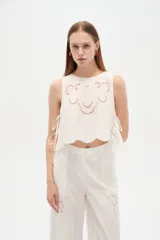 Musculosa de algodón color celeste, con cuello redondo y detalles bordados en tono blanco con diseño de broderie en la parte frontal. Cuenta con cordones laterales para ajustar.