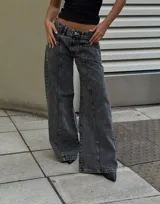 Pantalón de jean tipo wide leg con tiro bajo y lavado acid wash en tono gris oscuro. Presenta costuras verticales decorativas en el frente y bolsillos laterales.