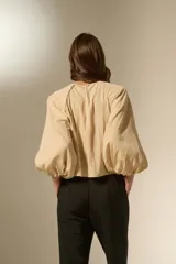 Blusa de color beige con cuello redondo y mangas largas abullonadas con puños elásticos. Presenta un corte holgado y fluido.