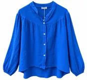 Camisa azul francia de manga larga abullonada con puños elásticos, cuello en V con escote mao y cierre frontal con botones blancos. Presenta diseño holgado y dobladillo asimétrico más largo en la parte trasera.
