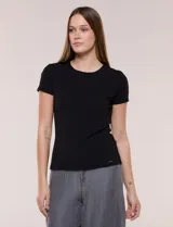 Remera básica de corte al cuerpo con textura acanalada, cuello redondo y mangas cortas. Presenta una pequeña placa metálica decorativa en el borde inferior.