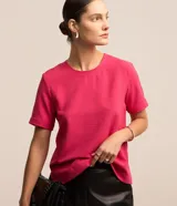 Blusa fucsia de manga corta con cuello redondo pespunteado, confeccionada en tejido de poliéster plano con efecto airflow y cierre posterior con botón.