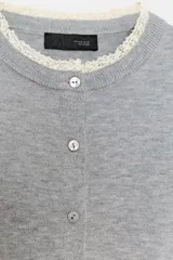 Chaqueta de punto de corte clásico, color gris, con cuello redondo y manga larga. Presenta cierre frontal con botones y detalles de puntilla en color crema en el cuello y los puños.