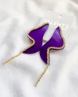 Par de caravanas colgantes de acrílico color violeta con forma irregular y borde con strass dorados.