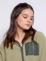 Campera polar color verde oliva, de corte largo, con cuello alto y cierre frontal. Tiene un bolsillo de nylon verde oscuro en el pecho y dos bolsillos laterales.