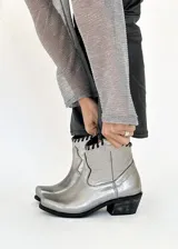 Botas texanas plateadas de cuero vacuno, con caña corta, taco bajo y detalle de tiento cosido a mano en la parte superior.