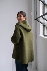 Tapado de paño color verde oliva con interior y detalles en beige. Presenta capucha amplia, cierre frontal, bolsillos laterales y mangas con puños vueltos que dejan ver el contraste de color.