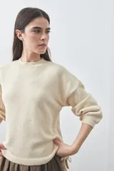 Sweater de tejido liviano con silueta relajada, hombros caídos y mangas largas con puños ajustados. Presenta cuello redondo y lazos ajustables en el bajo.