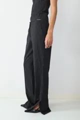 Pantalón de tiro medio color negro con raya diplomática, corte recto, bolsillos laterales con cierre y cierre frontal oculto. Presenta aberturas en los tobillos.