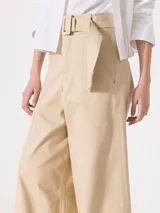 Pantalón de tiro alto color beige, de corte palazzo, con cinturón con hebilla forrada, bolsillos diagonales delanteros y bolsillos sastre traseros.