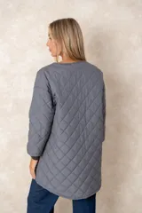 Campera acolchada de corte amplio y largo midi, color beige con diseño capitoneado. Presenta mangas tres cuartos con puños vueltos que revelan un interior estampado con motivo animal print. Diseño sin cuello y cierre frontal oculto.