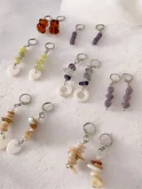 Par de aros colgantes con argollas tipo huggie de metal plateado. El diseño presenta una tira de piedras naturales irregulares en tonos verdes o crudos, finalizando en un dije de corazón de nácar o piedra clara.