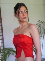 Top strapless color rojo vibrante, con frunces y pliegues que crean un efecto escultural y volumen en la parte delantera. Presenta un corte frontal con abertura central.