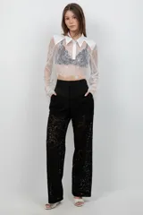 Camisa crop top de encaje blanco con mangas largas acampanadas, cuello camisero y pechera de tela lisa.
