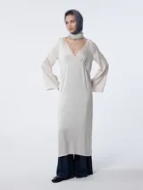 Vestido largo color crema, tipo túnica, confeccionado en crepé de satén de seda teñida en prenda. Tiene escote en pico con costura y ligeros fruncidos bajo el busto, líneas rectas y mangas acampanadas.