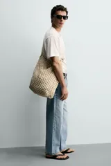 Bolso de hombro confeccionado en tejido trenzado de algodón con diseño de macramé, asa de hombro con detalle de nudo y bolsillo interior plano.