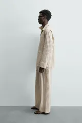 Camisa de calce relajado con diseño de rayas verticales, cuello bowling y manga larga. Cuenta con cierre frontal de botones y tres bolsillos de plastrón: uno en el pecho y dos en la cadera.