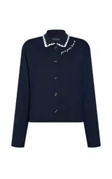 Cardigan de punto azul marino con cuello polo, cierre frontal de botones y detalle de bordado en el pecho. El cuello presenta un borde festoneado en color blanco.