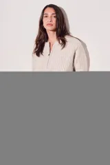 Sweater de punto color crema, con cuello redondo y cierre metálico a la mitad del frente.