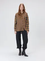 Camisa de viscosa con estampado geométrico en tonos tierra, de corte holgado y largo hasta la cadera. Presenta cuello clásico, cierre frontal con botones, bolsillo cuadrado en el pecho y puños estampados a juego.