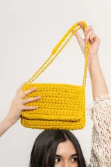Cartera bandolera tejida a crochet color amarillo, con correa de cadena dorada y forro interior.