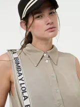 Vestido camisero corto color beige, sin mangas, con cuello clásico, cierre frontal con botones y bolsillos laterales.