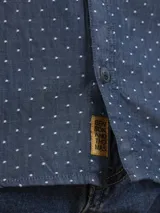Camisa de manga larga azul con pequeños lunares blancos, cuello clásico y bolsillo en el pecho.