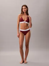 Conjunto de ropa interior Calvin Klein compuesto por un corpiño triangular y una bombacha colaless. Ambas piezas presentan un estampado de monograma de la marca en color rojo sobre fondo oscuro, con la banda elástica característica en color blanco con el logo de la marca en negro.